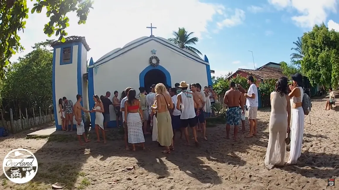 Devotos e turistas reunidos em frente à igreja para a Festa de Sao Sebastião Caraiva, celebrando a tradição na areia.