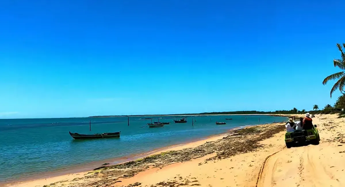 passeio de buggy Caraíva Corumbau na praia, com o veículo off-road de cor verde trafegando na areia à beira-mar sob o céu azul e água cristalina