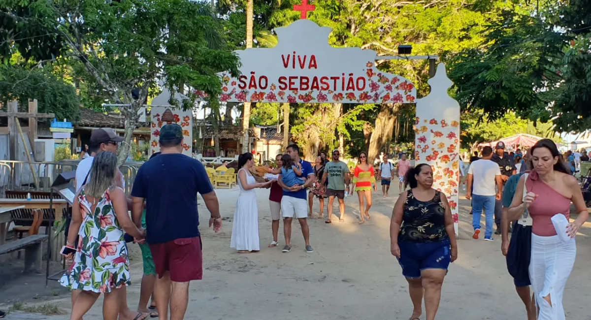 Entrada do Quadrado Histórico de Trancoso durante a Festa Folclórica de São Sebastião, mostrando um portal decorado "Viva São Sebastião" e pessoas caminhando na área de terra batida.